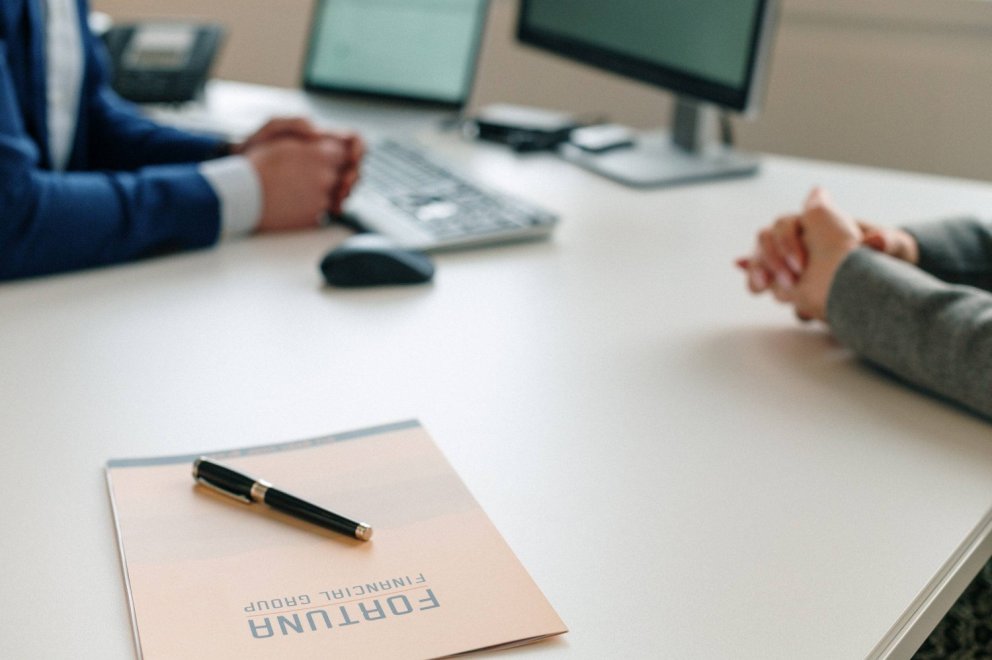 Een bureau met een notitieblok met de tekst "Fortuna Financial Group" en een pen, met de handen van twee mensen zichtbaar in een zakelijke omgeving.
