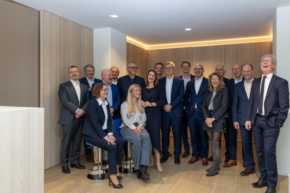 Het team van Fortuna Financial Group Antwerpen in formele kleding, lachend en poserend voor een lichte, moderne achtergrond in hun kantoor te Antwerpen.